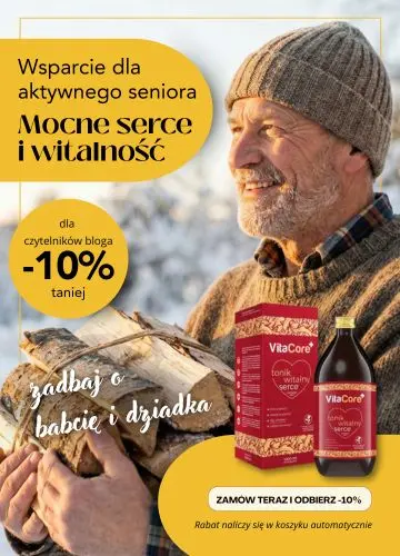 Uśmiechnięty senior niosący drewno w zimowej scenerii. Baner promocyjny VitaCore Tonik na serce i witalność – prezent na Dzień Dziadka z rabatem -10%